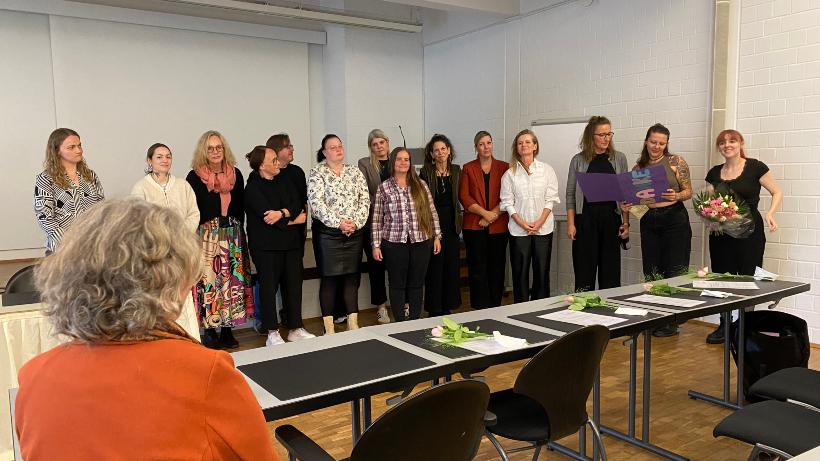 15 Teilnehmende stehen auf der Bühne und eine Dame sitzt im Auditorium davor.